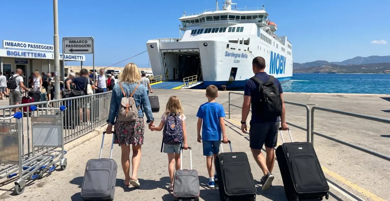 Eine Familie mit zwei Kindern steht mit Gepäck am sonnigen Fährhafen vor einem modernen weißen Fährschiff im Mittelmeer