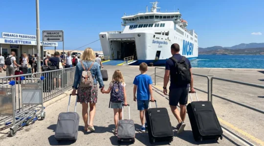 Eine Familie mit zwei Kindern steht mit Gepäck am sonnigen Fährhafen vor einem modernen weißen Fährschiff im Mittelmeer